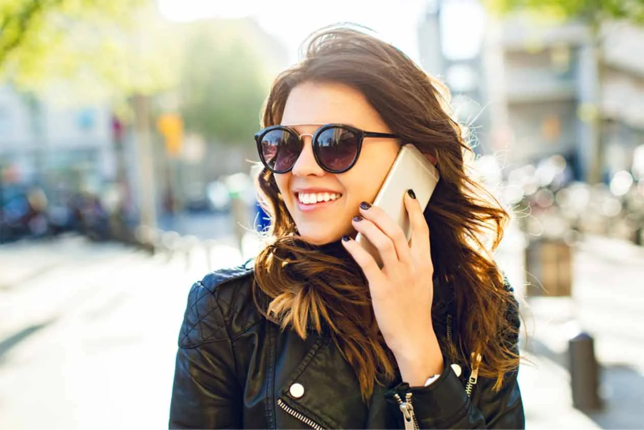 Młoda, uśmiechnięta kobieta na dworze rozmawia przez telefon