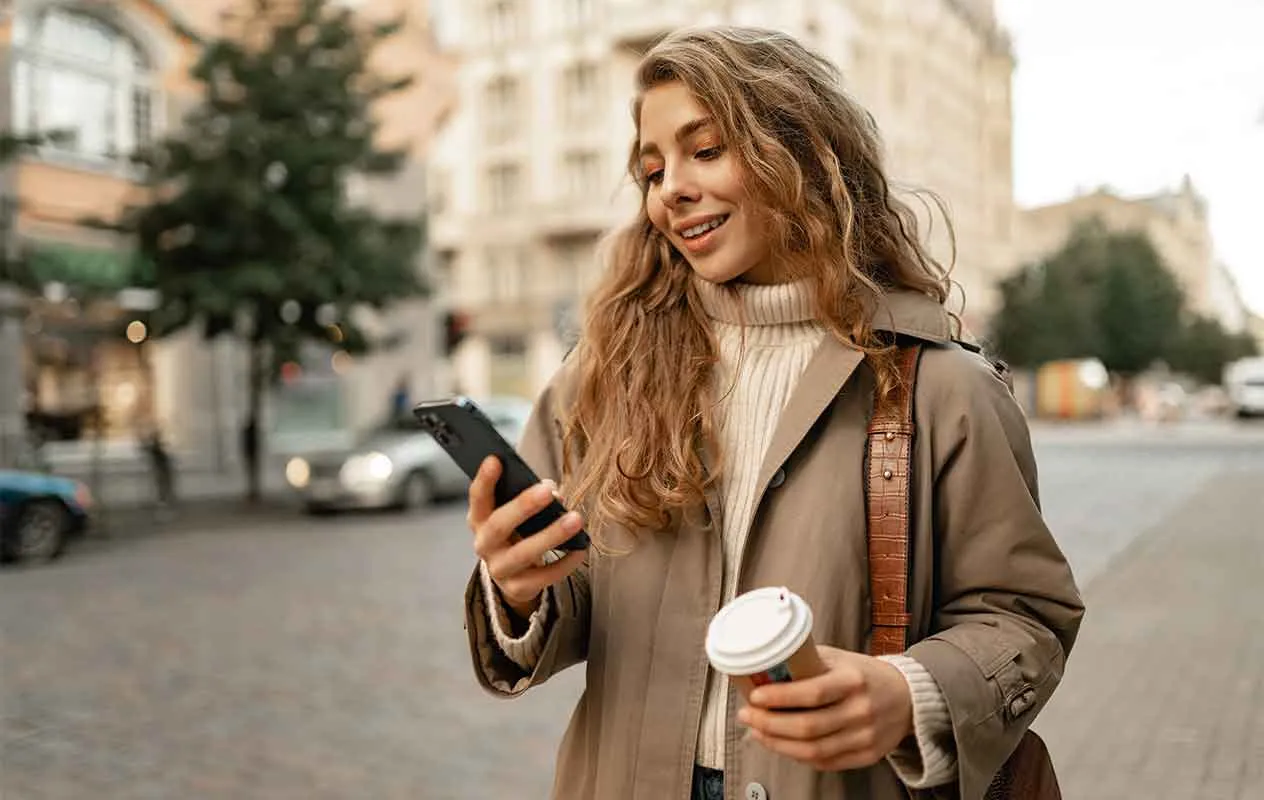 Kobieta z telefonem i kubkiem kawy korzysta z internetu mobilnego