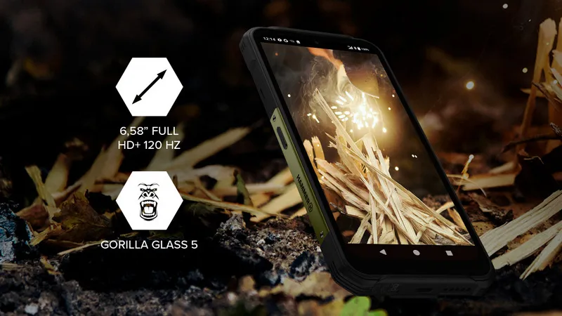 Wytrzymały smartfon leży na ziemi, a na jego ekranie widoczna jest scena z ogniskiem. Po lewej stronie znajdują się dwie sześciokątne ikony: pierwsza z symbolem strzałki i napisem 6,58 FULL HD+ 120 HZ, druga z wizerunkiem głowy goryla i napisem GORILLA GLASS 5.