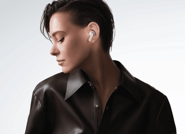Młoda kobieta w ciemnej koszuli z przekręconą na bok głową prezentuje słuchawkę Huawei FreeBuds Pro 5 w uchu