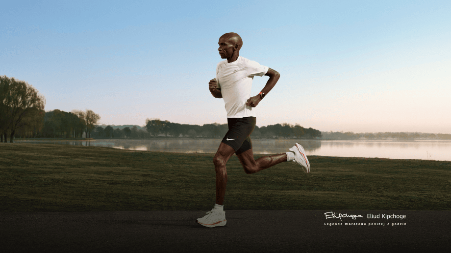 Legendarny maratończyk Eliud Kipchoge w trakcie biegu po trawie, na tle jeziora, na ręku ma Zegarek HUAWEI Watch Gt Runner 2