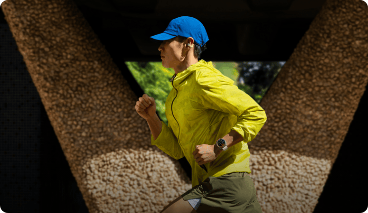 Mężczyzna w sportowym jaskrawym stroju i czapce w trakcie biegu, na tle budynku, na ręku ma zegarek HUAWEI Watch Gt Runner 2