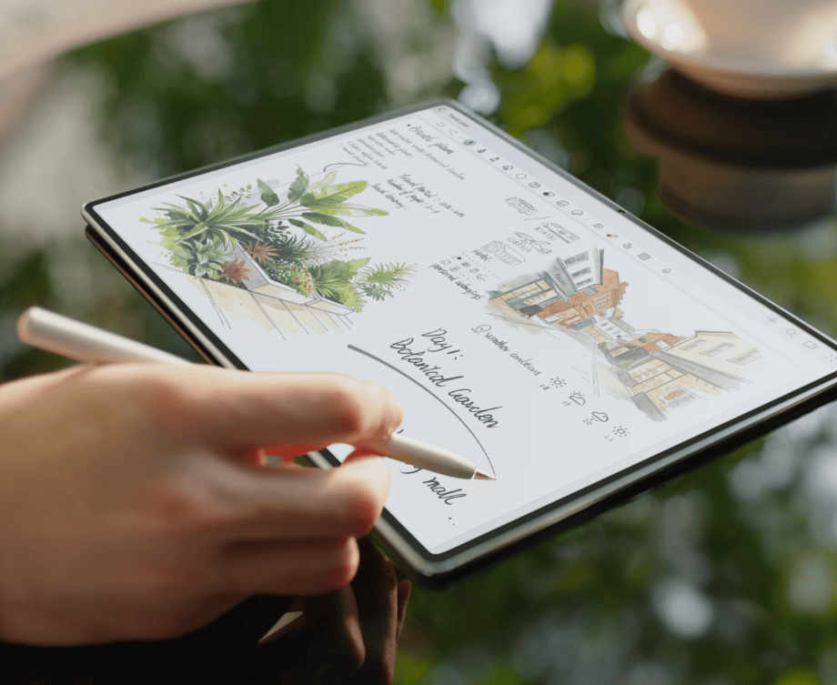 Tabletu HUAWEI MatePad Pro Max z kolorowymi grafikami leży na szklanym stole. Obok dłoń z rysikiem M-Pencil Pro.