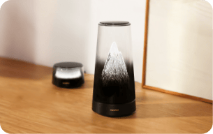 Router HUAWEI Mesh X3 Pro Suite wraz ze wzmacniaczem sygnału, na brązowej podłodze, na tle białej ściany, świecą na srebrno.