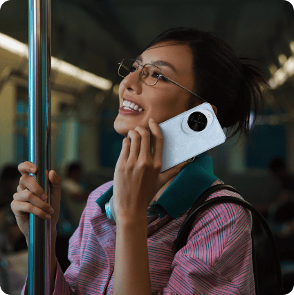 Stojąca w metrze, kobieta w kolorowej bluzce i o azjatyckich rysach trzyma przy uchu niebieski smartfon Huawei Nova 14 pro