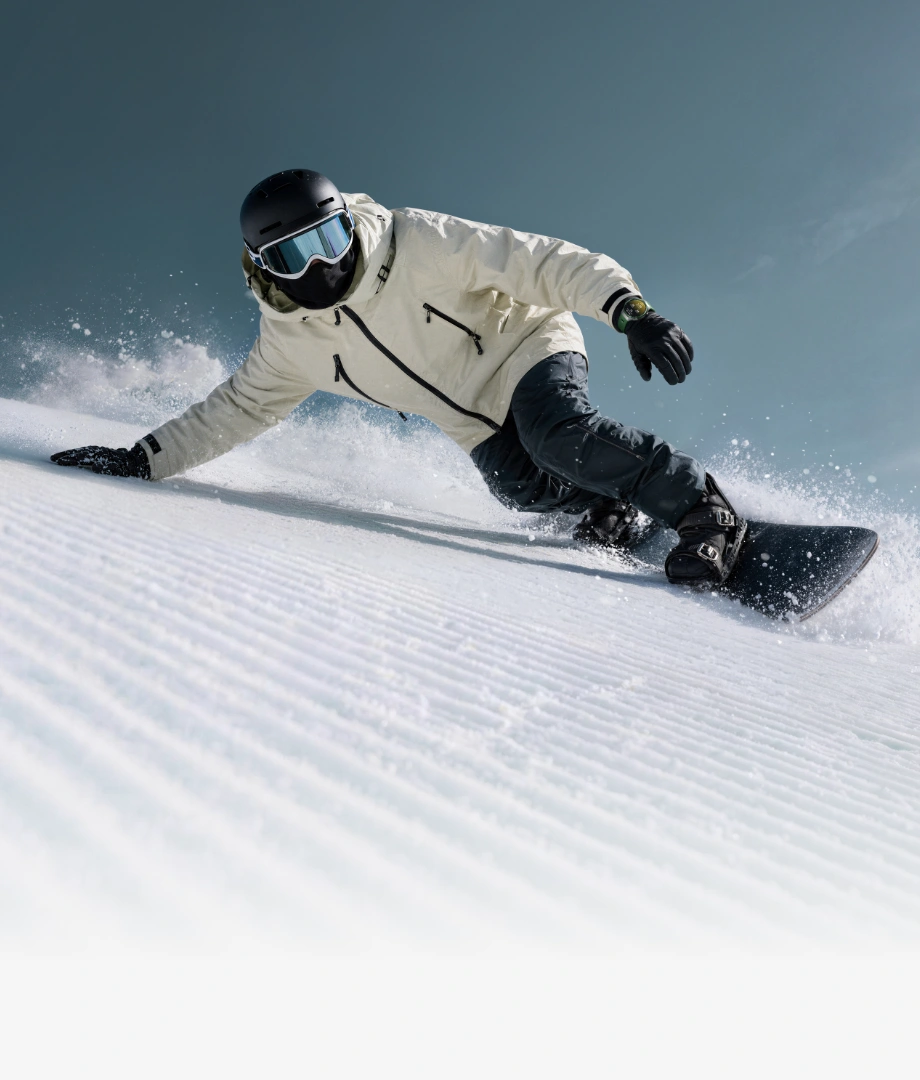Mężczyzna w kasku i goglach sunie na snowboardzie dotykając dłonią ośnieżony stok, na ręku ma zegarek Huawei Watch GT 7 Pro