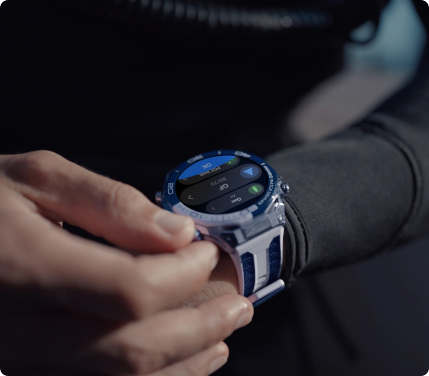 Zbliżenie na nadgarstek osoby w piance nurkowej, która obsługuje dotykiem smartwatch HUAWEI w srebrno-niebieskiej kopercie z granatowym paskiem.