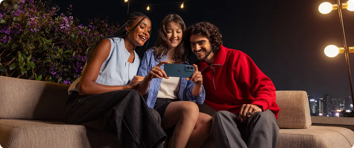 Grupa znajomych oglądająca treści na smartfonie Motorola moto g06 POWER na tarasie nocą