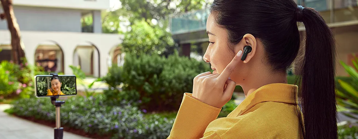 Kobieta w czarnych słuchawkach OPPO rozmawia przez telefon na statywie w plenerze.