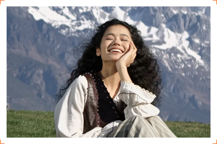 Uśmiechnięta kobieta siedząca na trawie na tle ośnieżonych gór