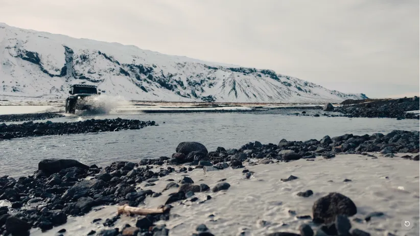 Terenowy samochód przekraczający rzekę na tle zaśnieżonych gór zimą