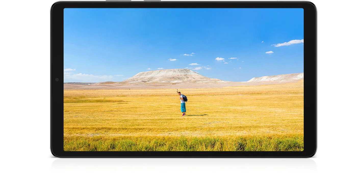 Galaxy Tab A11+ jest umieszczony poziomo, wyświetlając wyraźny obraz mężczyzny machającego rękami, co sugeruje swobodny nastrój. W tle błękitne niebo rozciąga się nad szerokim horyzontem żółto-brązowej trawy. Pod tabletem znajduje się napis „Częstotliwość odświeżania 90 Hz”.