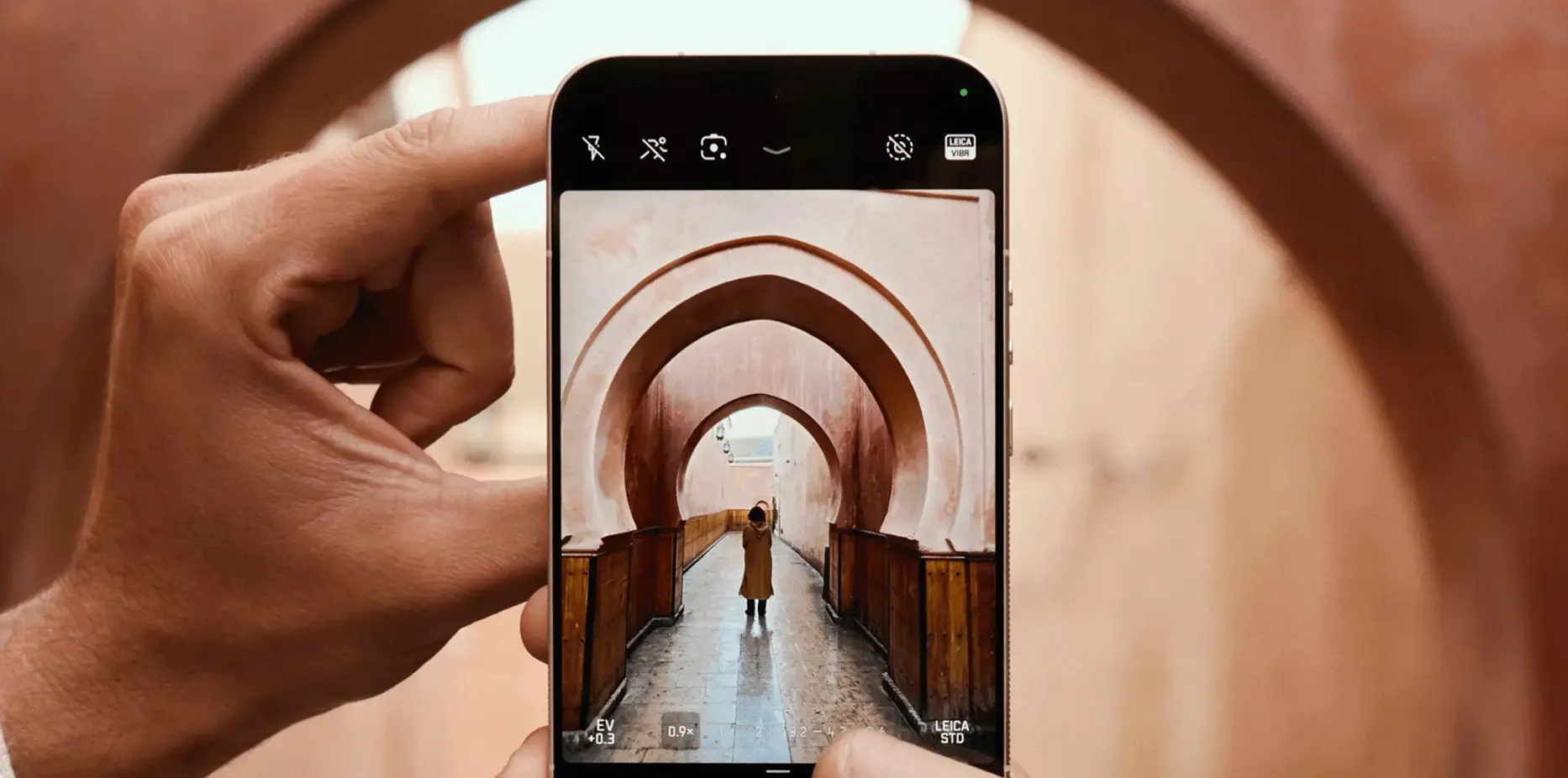 Leitzphone w dłoniach fotografuje osobę stojącą w łukowym przejściu, podgląd kadru na ekranie