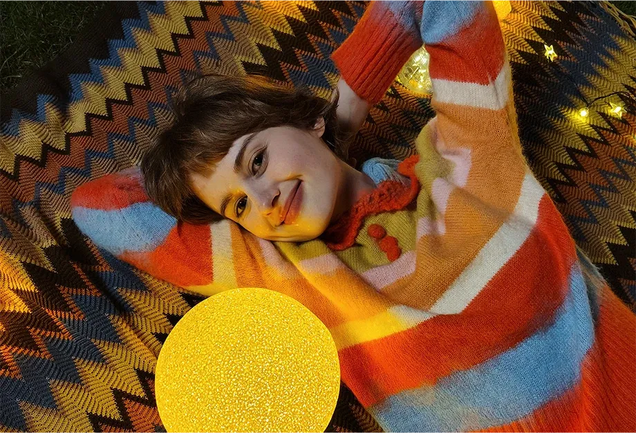 Portret kobiety leżącej na kocu obok świecącej lampy, zdjęcie w ciepłym świetle
