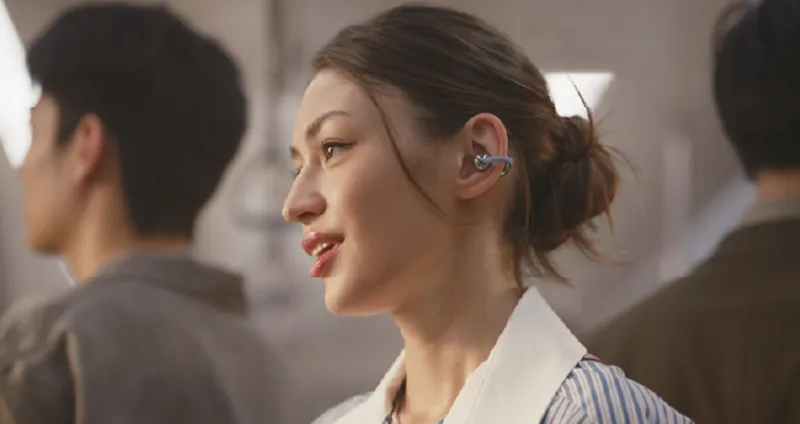 Kobieta rozmawiająca w tłumie, nosi słuchawki Huawei FreeClip zapewniające wyraźne rozmowy.