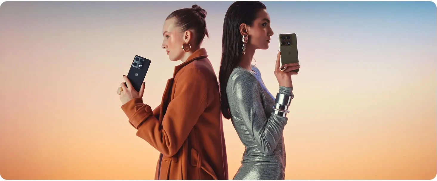 Dwie elegancko ubrane kobiety stojące plecami do siebie i trzymające smartfony motorola signature w dłoniach